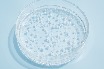 Transparent drops of cosmetic product serum gel in petri dish. Liquid texture with bubbles on blue...
