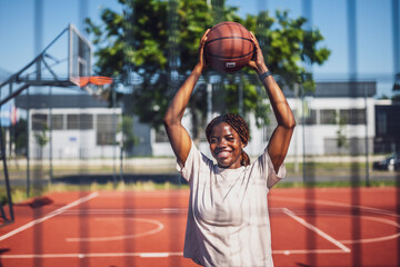 Naklejka premium African American female player holding a ball and laughing during summer training session. Active lifestyle and city sport vibes.