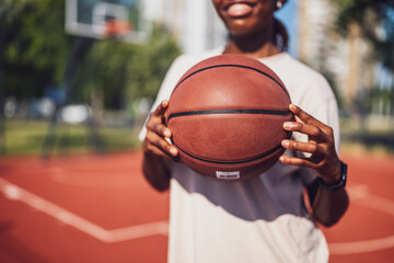 Close up of young woman holding basketball. She is practicing basketball on sunny day.