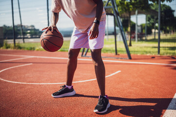 Young black woman practicing basketball alone at sports court in the morning. She is dribbling the...