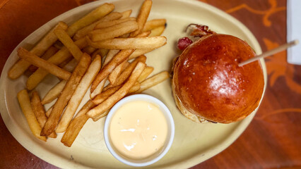 A delicious burger with a golden brioche bun, accompanied by crispy fries and a side of creamy dipping sauce.