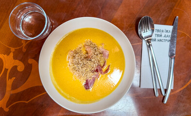 A vibrant orange soup garnished with crispy toppings served on a wooden table.