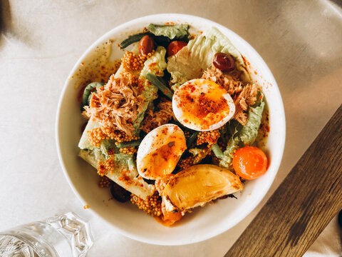 A vibrant mixed salad bowl featuring greens, boiled eggs, and tuna, garnished with spices and served in a rustic dish.