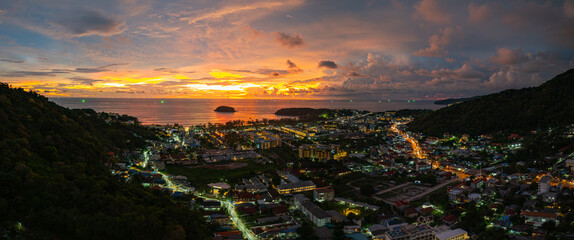 A breathtaking sunset paints the sky in vivid hues of orange and blue over a coastal town, with...