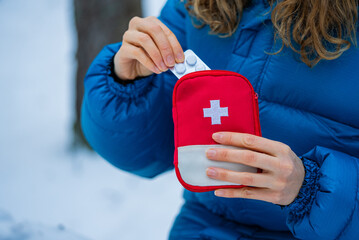 Winter hiker wearing blue jacket extracting medication from red first aid kit while navigating...