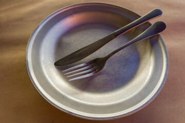 Empty shallow aluminum plate with stainless steel fork and knife