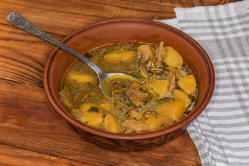 Boletus soup in clay bowl with spoon on rustic table