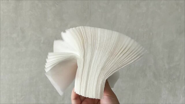Stack white napkins in hand on white background isolation. Paper napkins with female hand. Stack of clean paper napkins.