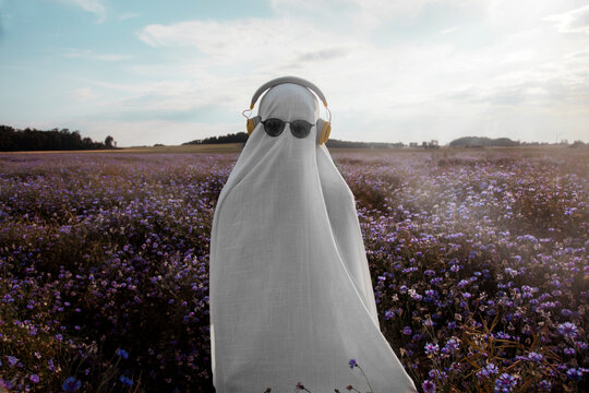 Ghost with sunglasses and headphones relaxing in summer purple flower meadow