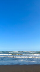 A peaceful beach scene with gentle waves meeting the sandy shore beneath a clear blue sky. The calm...