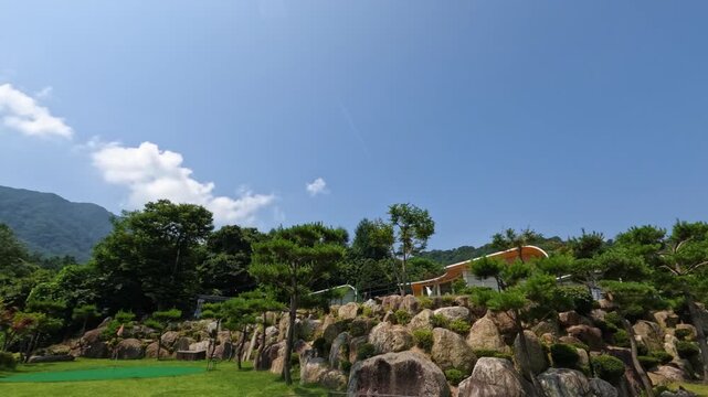 A beautiful time-lapse on a clear sunny day at a luxury glamping resort in Gapyeong, showing clouds moving across a blue sky above a landscaped rock garden and mountain.