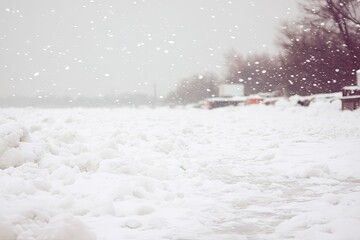 Snowy riverbank scene. Light snowfall blankets a snowy riverbank with ice chunks.  Distant vehicles are visible