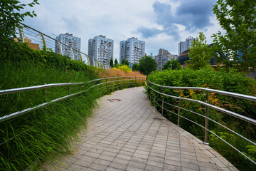 Curved paved walkway with modern metal railings, flanked by lush green grass and bushes, leading...
