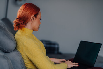 Focused young woman working remotely from home office using laptop