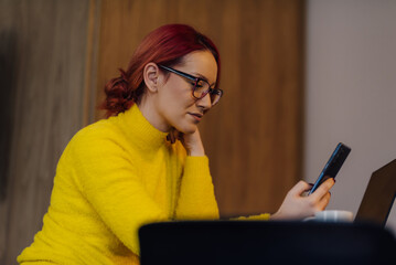 Focused freelancer working remotely using smartphone and laptop at home
