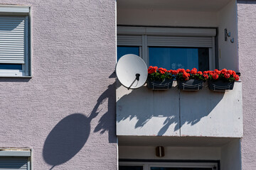Balcony with red flowers and satellite dish in daylight