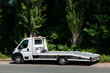 White flatbed tow truck parked beside green trees
