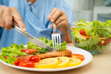 Asian elderly woman patient eating salmon stake and vegetable salad for healthy food in hospital.