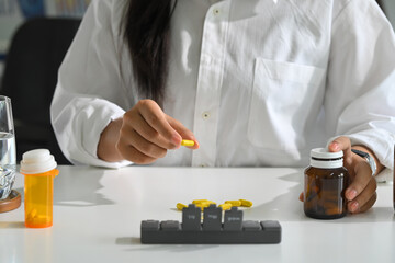 Woman organizing capsules into weekly pill box, daily medication management and routine