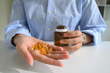 Close up of a person holding fish oil capsules in one hand. Health and nutrition concept