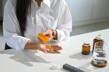 Woman pouring yellow capsules from a pill bottle into her hand. Health care concept