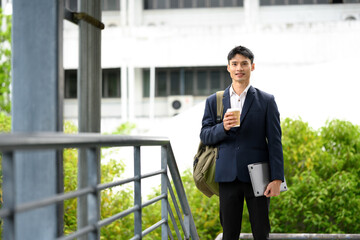 Businessman standing outdoors with coffee and laptop, ready for a productive day