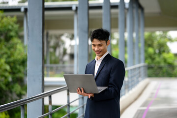 Smiling businessman working on a laptop outdoors on a pedestrian bridge