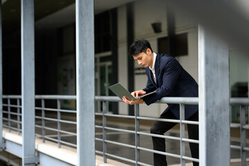 Smiling businessman working on a laptop outdoors on a pedestrian bridge