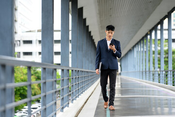 Businessman walking confidently on pedestrian bridge while checking smartphone