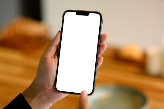 Close up of hands holding smartphone with blank screen in a warm kitchen