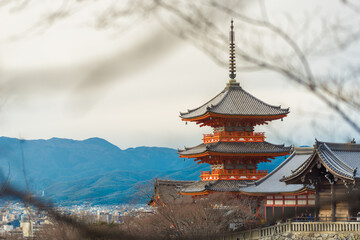 three-tiered pagoda Kiyomizu-dera Temple,Kyoto frame by bare winter branch. bright vermilion tone of temple with soft blue sky and distant mountain.Quiet elegance of tradition Japanese architecture 