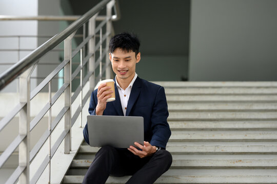Businessman sitting on stairs sipping takeaway coffee and using laptop