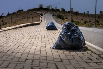 Two black garbage bags on paved road in barren landscape. scene highlights environmental issues and...