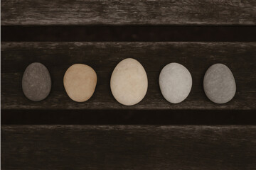 Oval - shaped stones placed on a dark wooden surface.
