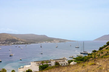 A scenic view of a calm bay with several boats anchored. Rolling hills and a clear sky create a...