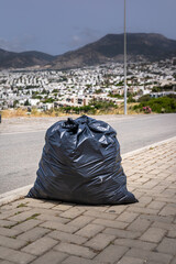  black garbage bag on a paved road in a barren landscape. scene highlights environmental issues and...