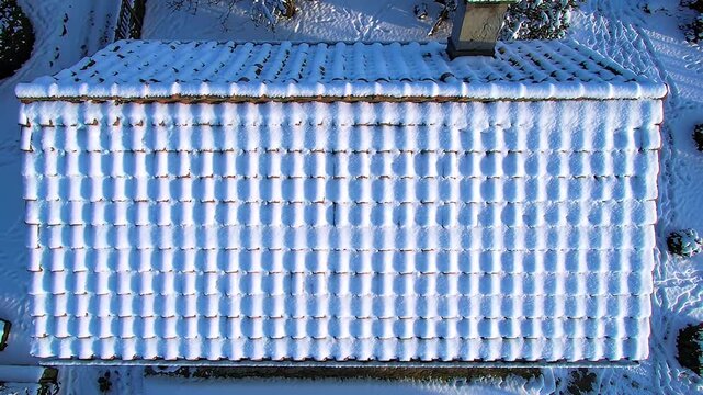 Snowy roof with repetitive tiles and a single chimney, aerial perspective