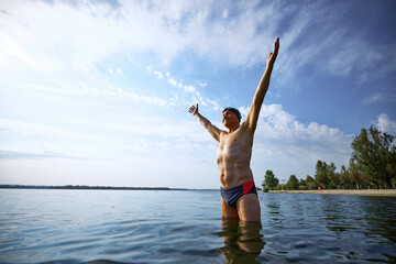 Happy elderly swimmer raising arms triumphantly in lake. Concept of summer sport, achievement,...