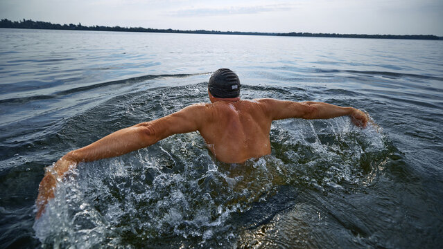 Senior swimmer from behind doing butterfly stroke in open water. Concept of summer sport, active aging, senior endurance, fitness resilience, adult wellness, and mature lifestyle motivation. - Powered by Adobe