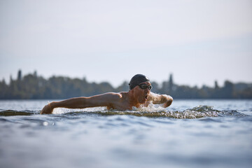Focused senior man swimming butterfly stroke in lake. Concept of strength in later age, endurance,...