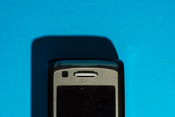Top part of old mobile phone casting shadow on bright blue background. Bold retro composition. High...