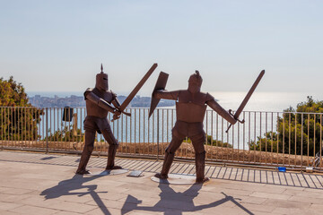 Two metal sculptures of knights engaged in a mock sword fight overlook the Mediterranean Sea at...