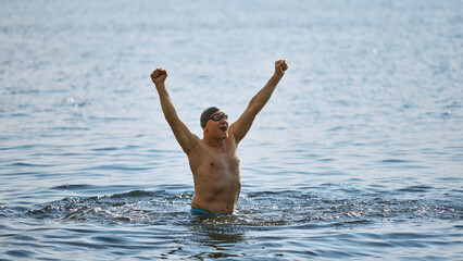 Senior swimmer celebrating victory with raised fists in lake. Concept of aging success, mature...