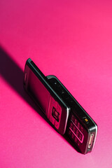 Retro black slider phone standing on a vibrant pink background in dramatic light. Nostalgic pop-art composition. High quality photo