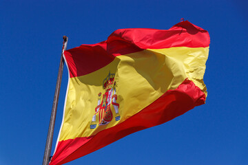 The national flag of Spain waving proudly against a clear blue sky, representing Spanish culture...