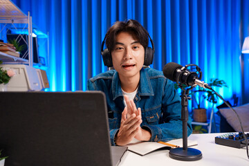 Smiling man podcaster make audio podcast with headphones and microphone in modern home studio.