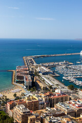 Naklejka premium A panoramic view of Alicante's coastline featuring picturesque beaches, bustling marina, and vibrant urban architecture under clear blue skies. Ideal for travel and lifestyle applications.