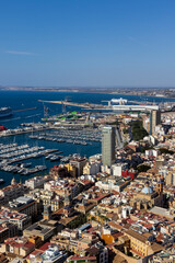 Fototapeta premium A panoramic view of Alicante, showcasing the bustling harbor, vibrant cityscape, and clear blue sky, illustrating maritime activities and urban life.