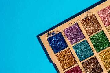 Messy glitter eyeshadow palette on bold cyan background. Imperfect beauty in vibrant pop style. High quality photo