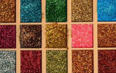 Close-up of colorful glitter eyeshadows in used palette. Textured beauty concept with bold sparkle. High quality photo